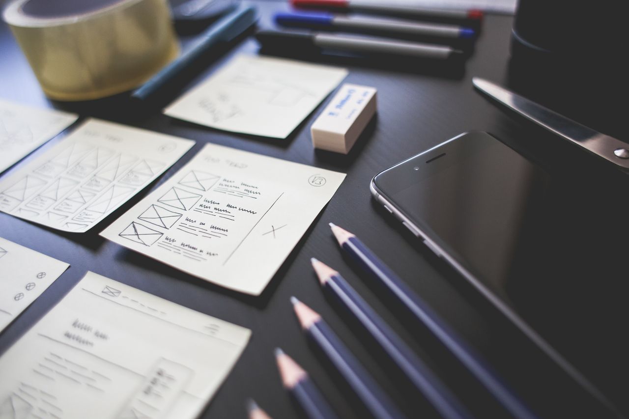 Un espace de travail créatif présentant des maquettes de design UI, des crayons, un smartphone et d’autres outils de bureau.
